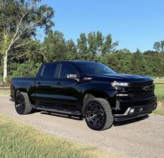 a black truck parked on the side of a dirt road next to grass and trees