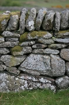 an old stone wall with moss growing on the rocks and grass in the foreground