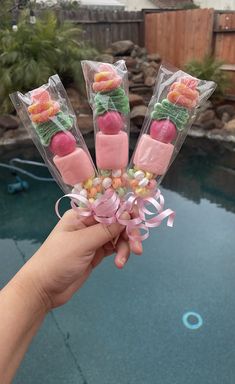 someone is holding up some candy sticks with flowers on them in front of a pool
