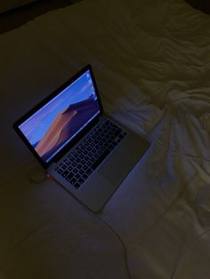an open laptop computer sitting on top of a white bed covered in blankets and pillows