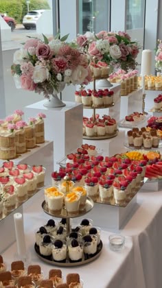 an assortment of desserts are displayed on a table with flowers in vases behind them