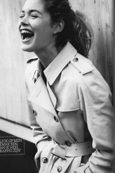 a black and white photo of a woman in trench coat smiling with her mouth open