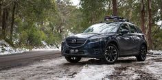 the mazda cx - 5 is driving on a snowy road with trees in the background