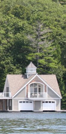 a large house sitting on top of a lake next to a lush green tree covered hillside