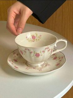 a person is holding a cup and saucer on top of a white round table