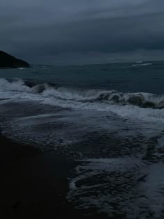 the ocean is dark and stormy with waves crashing on it's shore, as seen from an empty beach