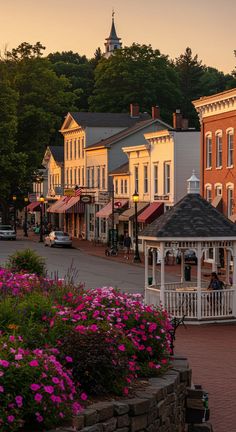 a small white gazebo sitting in the middle of a street next to flowers and buildings