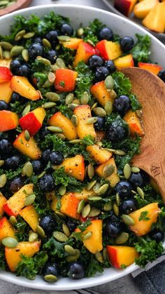 a salad with blueberries, kale and pineapples in a white bowl