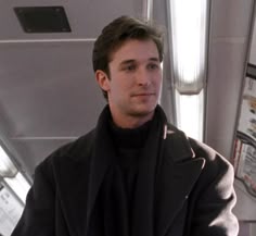 a man in a black coat and scarf on a bus looking at the camera,