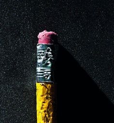 a yellow and black pencil with pink crayons on the end in front of a black background