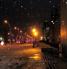 a city street at night with snow falling on the ground and buildings in the background