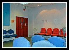 an empty waiting room with blue chairs and red seats in front of the door,