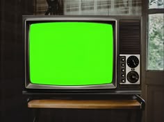 an old television with a green screen sitting on a table in front of a window