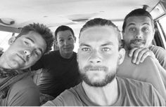 four men are sitting in the back of a car and one is looking at the camera
