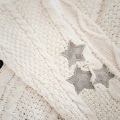 two silver stars on a white knitted sweater with black furnishing next to it