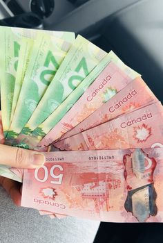 a person is holding several canadian money in their hand