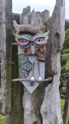 an owl mask is hanging on the side of a wooden fence post in front of some trees