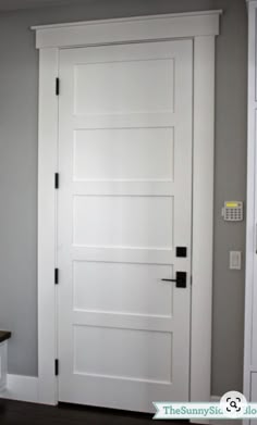 a white door in the corner of a room with gray walls and wood flooring