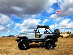an old jeep is parked in a field with the american flag on it's roof