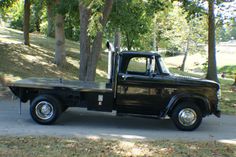 a black truck parked on the side of a road next to some trees and grass
