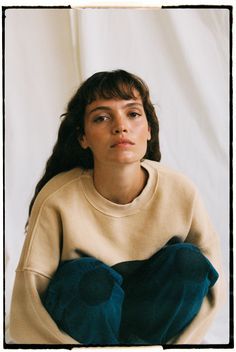 a woman sitting on the ground with her hands in her pockets and looking off to the side