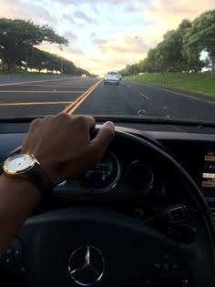 a person is driving their car down the road with his hand on the steering wheel