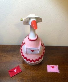 a duck in a dress and hat sitting on a table next to two small hearts