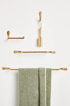 three gold towel hooks and two green towels hanging on the wall next to each other