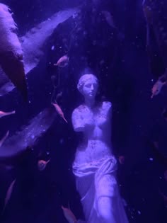 a woman in white dress standing next to an aquarium filled with fish and corals