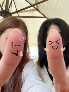 two girls with faces painted on their fingers, one holding up the other's thumb