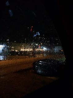rain is falling on the windshield of a car at night time with lights in the background