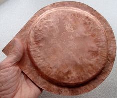 a hand holding an old copper plate on a table