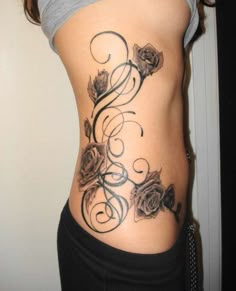 a woman's stomach with roses and swirls tattoo on the side of her body