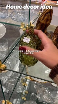 a hand is holding a glass bottle in front of some gold and silver items on display