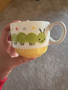 a person holding up a cup with the very cute caterpillar design on it