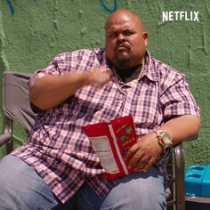 a man sitting in a chair holding a book and pointing to the side with his hand