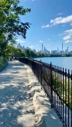 a black fence along the side of a road next to a body of water with buildings in the background