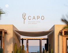 an entrance to a resort with cactus trees and the ocean in the background