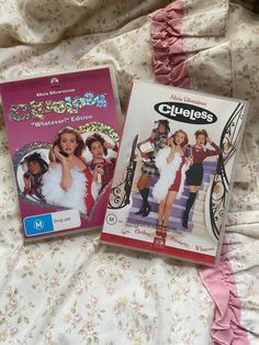 two dvd's sitting on top of a bed covered in pink and white sheets