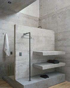 a bathroom with concrete walls and steps leading up to the shower area, along with black shoes on the floor