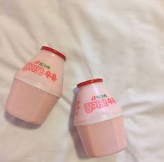 two pink cups sitting on top of a white bed next to each other with writing on them