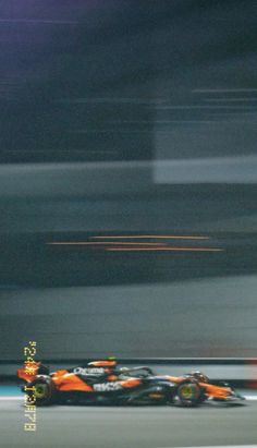 an orange race car driving down the track with blurry lights in the back ground