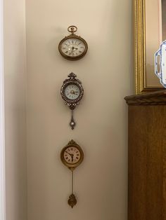 three clocks are hanging on the wall next to a mirror