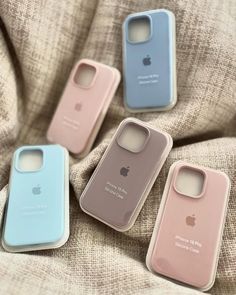 four iphone cases sitting on top of a bed next to an apple phone case in blue, pink and white