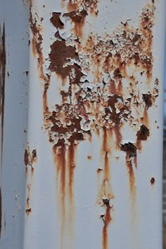 an old rusted metal pole with white paint and brown spots on the top part