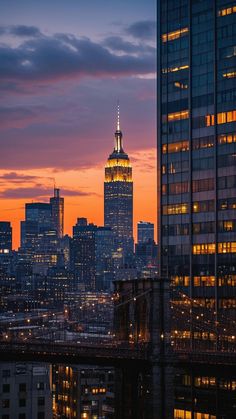 the empire building is lit up at night in new york city, with other skyscrapers behind it