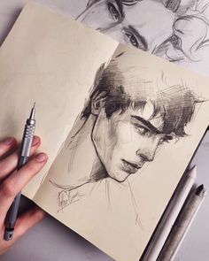 a hand holding a pen over a drawing book with two drawings on the pages and another person's head