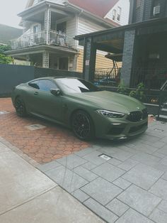 a green sports car parked in front of a house next to a brick walkway and fence