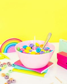 a pink bowl filled with lots of candy next to rainbow colored paper clips and scissors