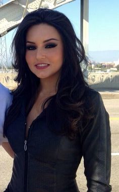 a beautiful woman standing next to a man in a black leather jacket and tie on top of a bridge